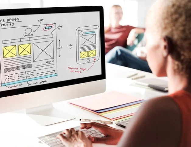 Web designer reviewing a website wireframe sketch on an iMac.