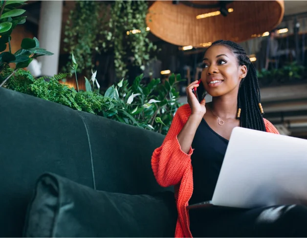 Woman sitting on a couch in a restaurant, discussing her business and website goals over the phone with a web designer.